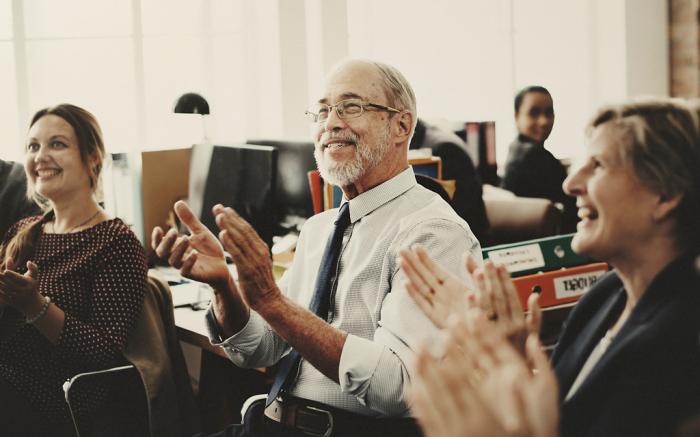 old man clapping in office with colleagues 