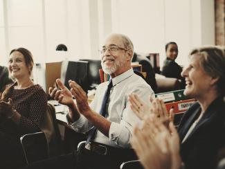 old man clapping in office with colleagues